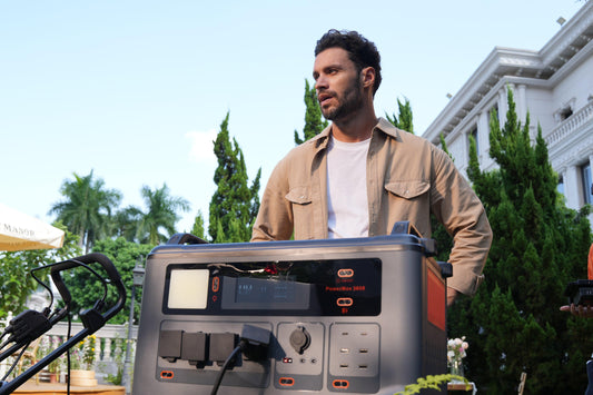 Man outdoors with portable solar power generator, plugs and lush greenery in background