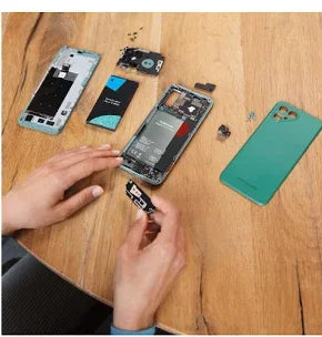 Hands repairing a smartphone with parts on a wooden table, renewable energy concept.
