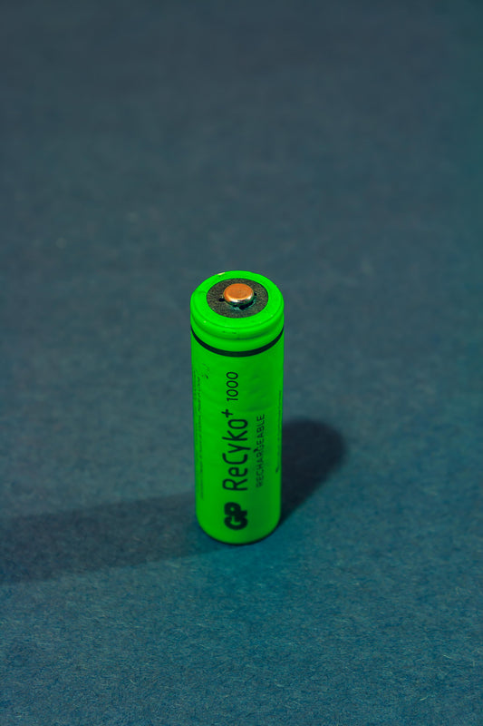 Green rechargeable coin battery standing upright on a dark surface.