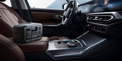 Portable BLUETTI Elite 30 V2 power station sits on a brown leather car seat, displaying its control panel and connections.