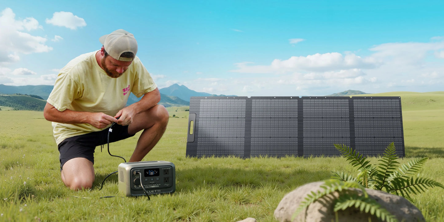 Portable BLUETTI Elite 30 V2 power station is set up on grass, with a user connecting it to solar panels in the background.