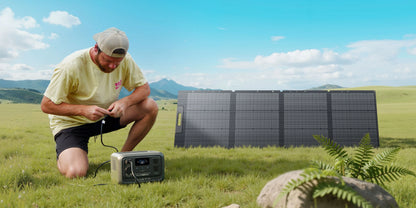 Portable BLUETTI Elite 30 V2 power station is set up on grass, with a user connecting it to solar panels in the background.