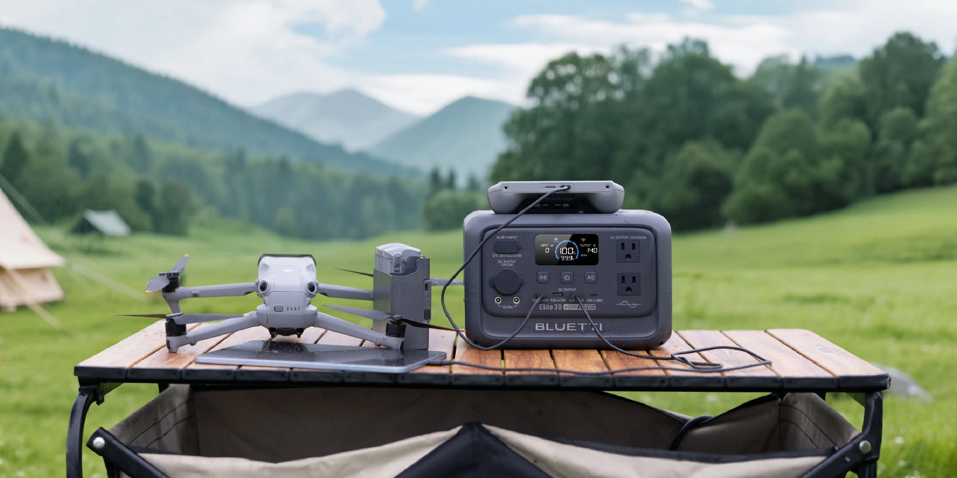 BLUETTI Elite 30 V2 portable power station in grey, displayed on a wooden table with a drone, set in a green outdoor landscape.