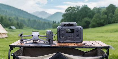 BLUETTI Elite 30 V2 portable power station in grey, displayed on a wooden table with a drone, set in a green outdoor landscape.