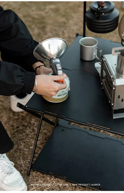 Person preparing coffee outdoors with a portable coffee maker and funnel.