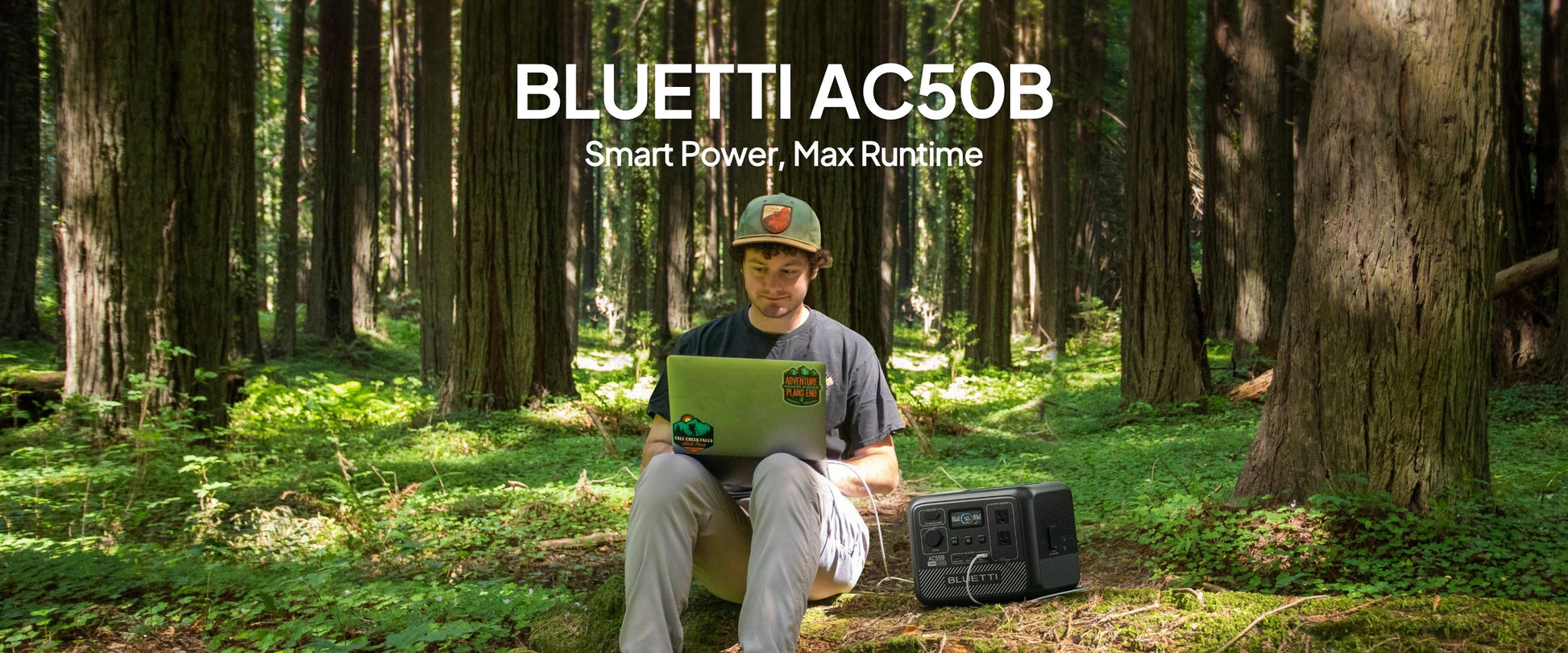 A person sitting on the forest floor uses a laptop connected to the BLUETTI AC50B portable power station beside them.