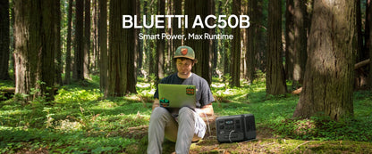 A person sitting on the forest floor uses a laptop connected to the BLUETTI AC50B portable power station beside them.